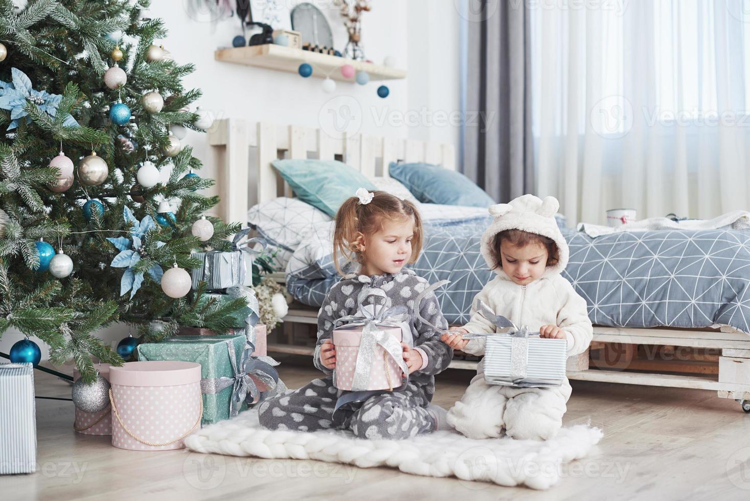 dos hermanitas abren sus regalos en el árbol de navidad por la mañana en la terraza foto