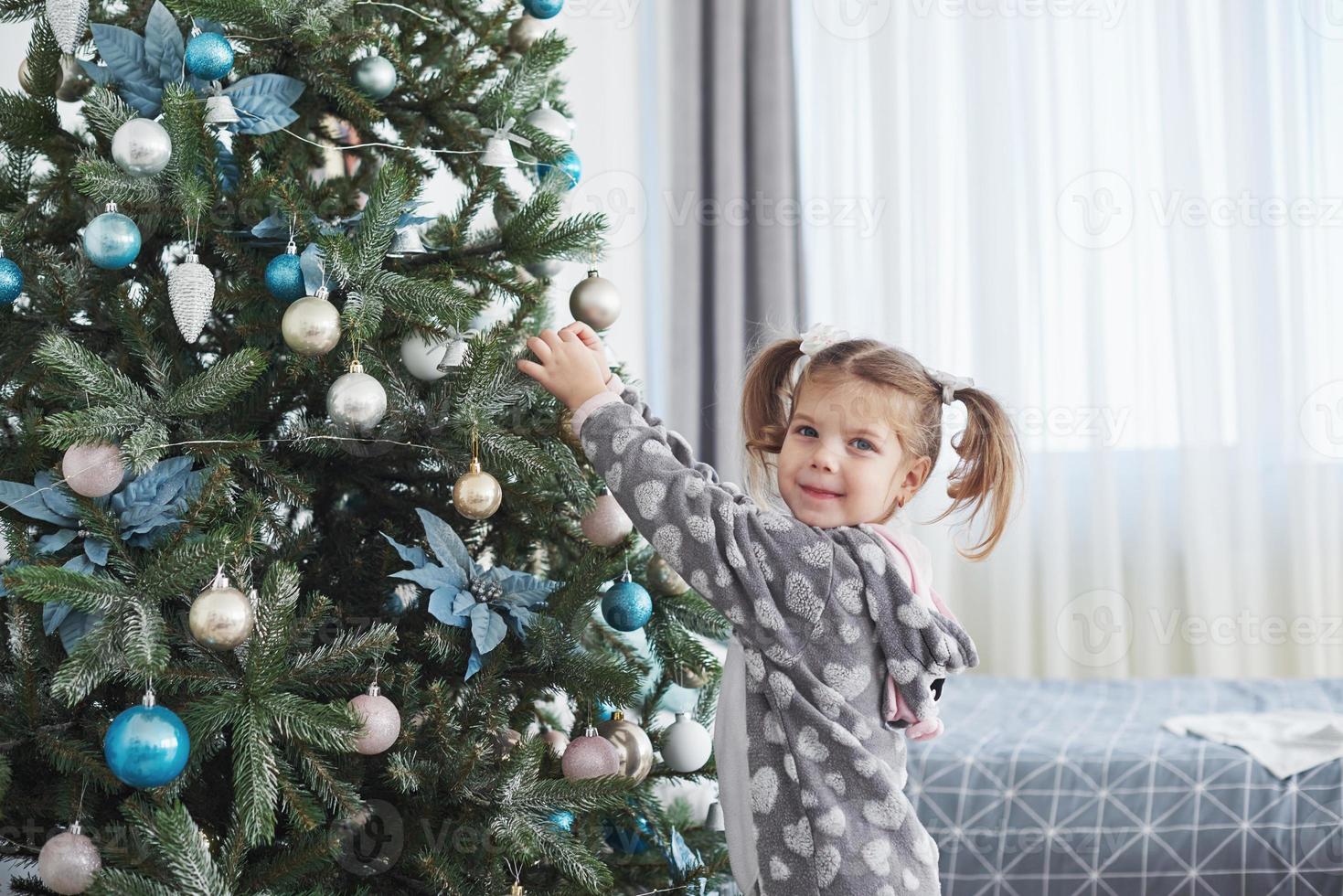Merry Christmas and Happy Holidays. Young girl helping decorating the Christmas tree, holding some Christmas baubles in her hand photo