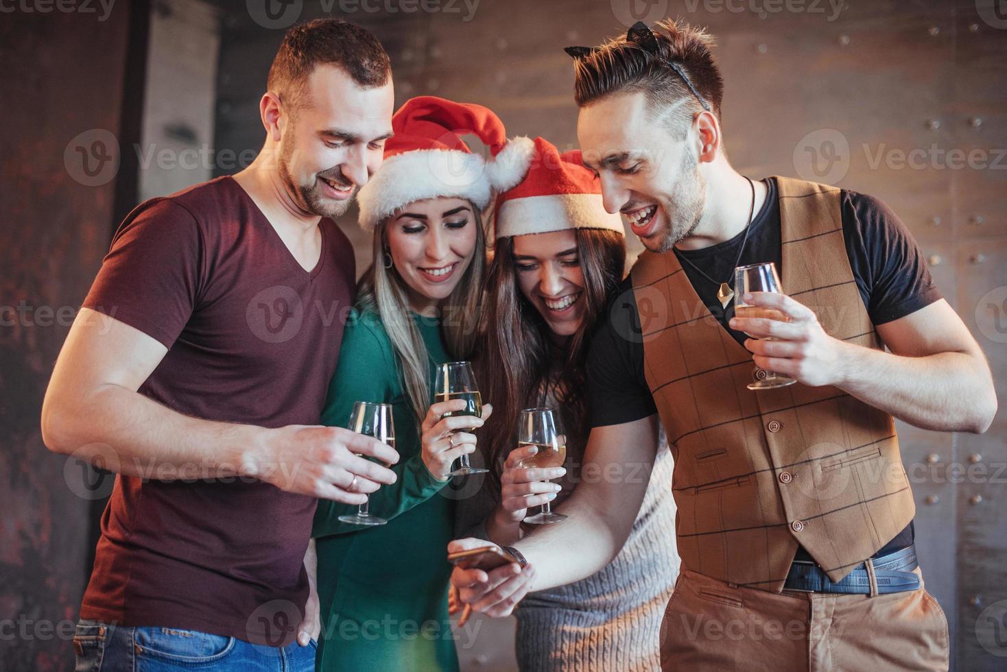 alegres viejos amigos se comunican entre sí y miran el teléfono, con copas de champán en la fiesta de año nuevo. concepto de entretenimiento y estilo de vida. personas conectadas wifi foto