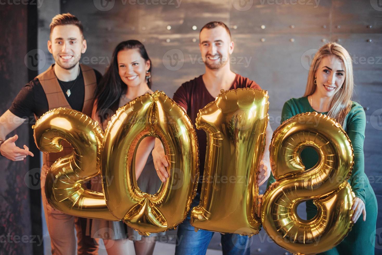 dos hermosas parejas jóvenes divirtiéndose en la fiesta de fin de año, con números de cartón 2018 foto