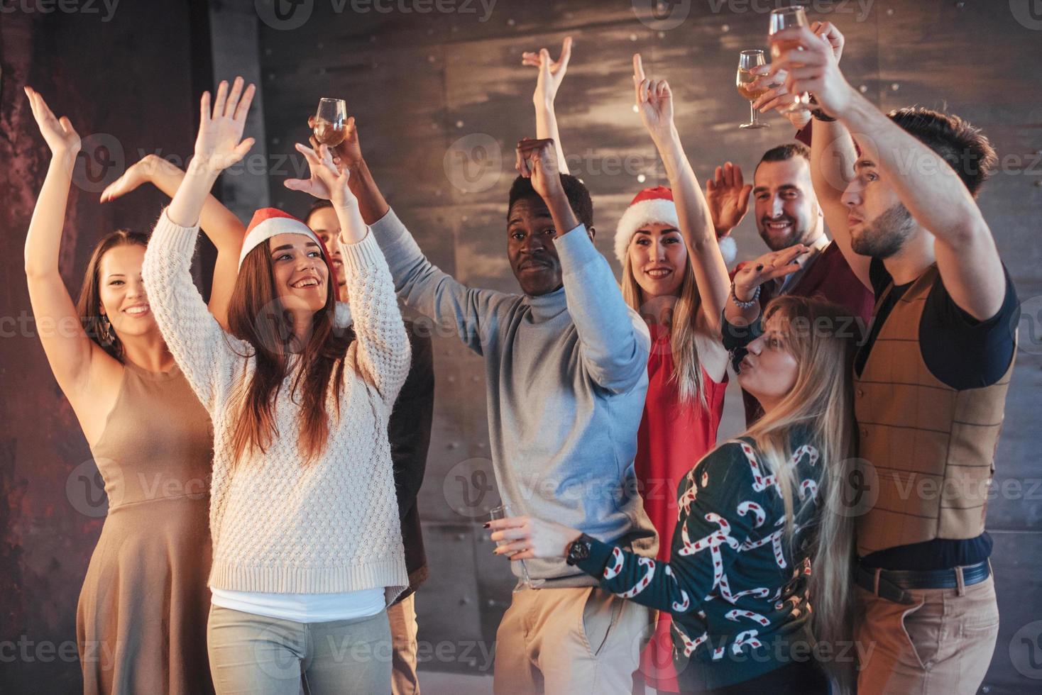 fiesta con amigos. aman la navidad. grupo de jóvenes alegres que llevan bengalas y copas de champán bailando en la fiesta de año nuevo y mirando felices. conceptos sobre el estilo de vida de la unión foto