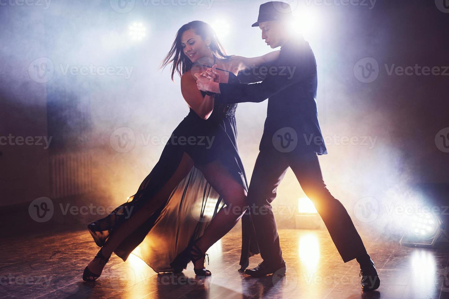 hábiles bailarines actuando en la habitación oscura bajo la luz y el humo del concierto. pareja sensual realizando una danza contemporánea artística y emocional foto