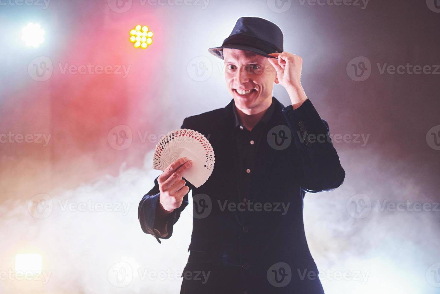 Magician showing trick with playing cards. Magic or dexterity, circus, gambling. Prestidigitator in dark room with fog photo