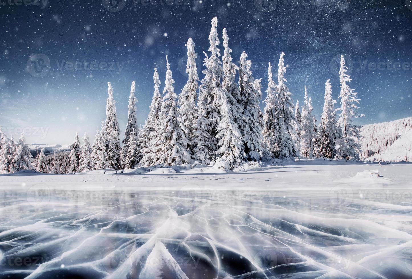 Blue ice and cracks on the surface of the ice. Frozen lake in winter mountains. It is snowing. The hills of pines. Winter. Carpathian Ukraine Europe photo