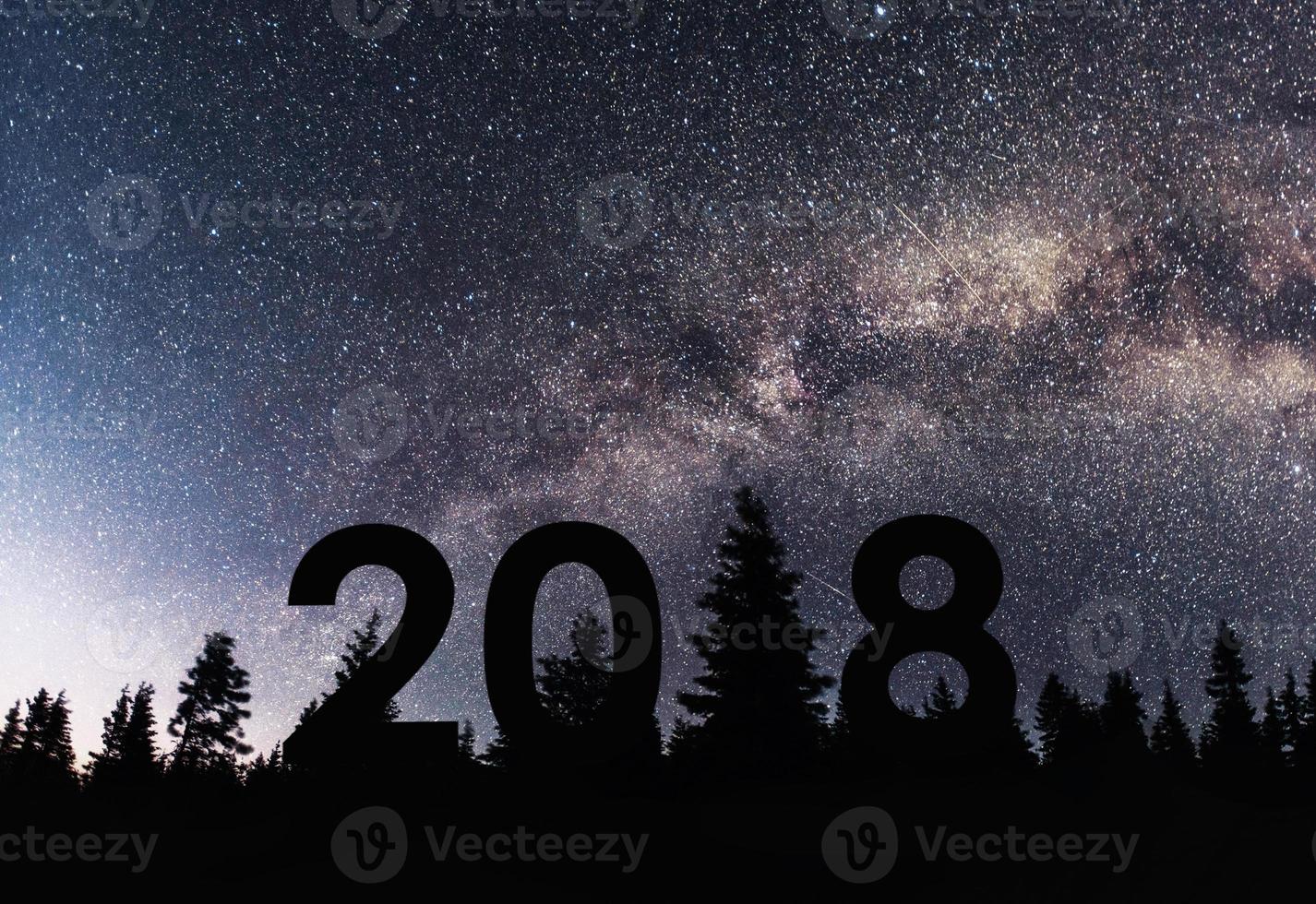 feliz por el fondo de año nuevo 2018 de la galaxia de la vía láctea en un tono de cielo oscuro de estrella brillante sobre siluetas de pinos foto