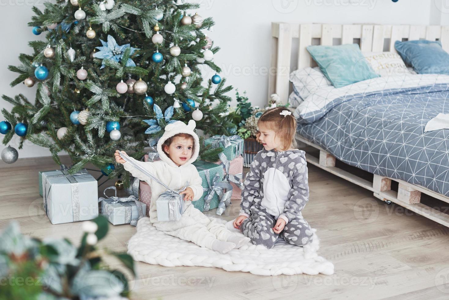 dos hermanitas abren sus regalos en el árbol de navidad por la mañana en la terraza foto