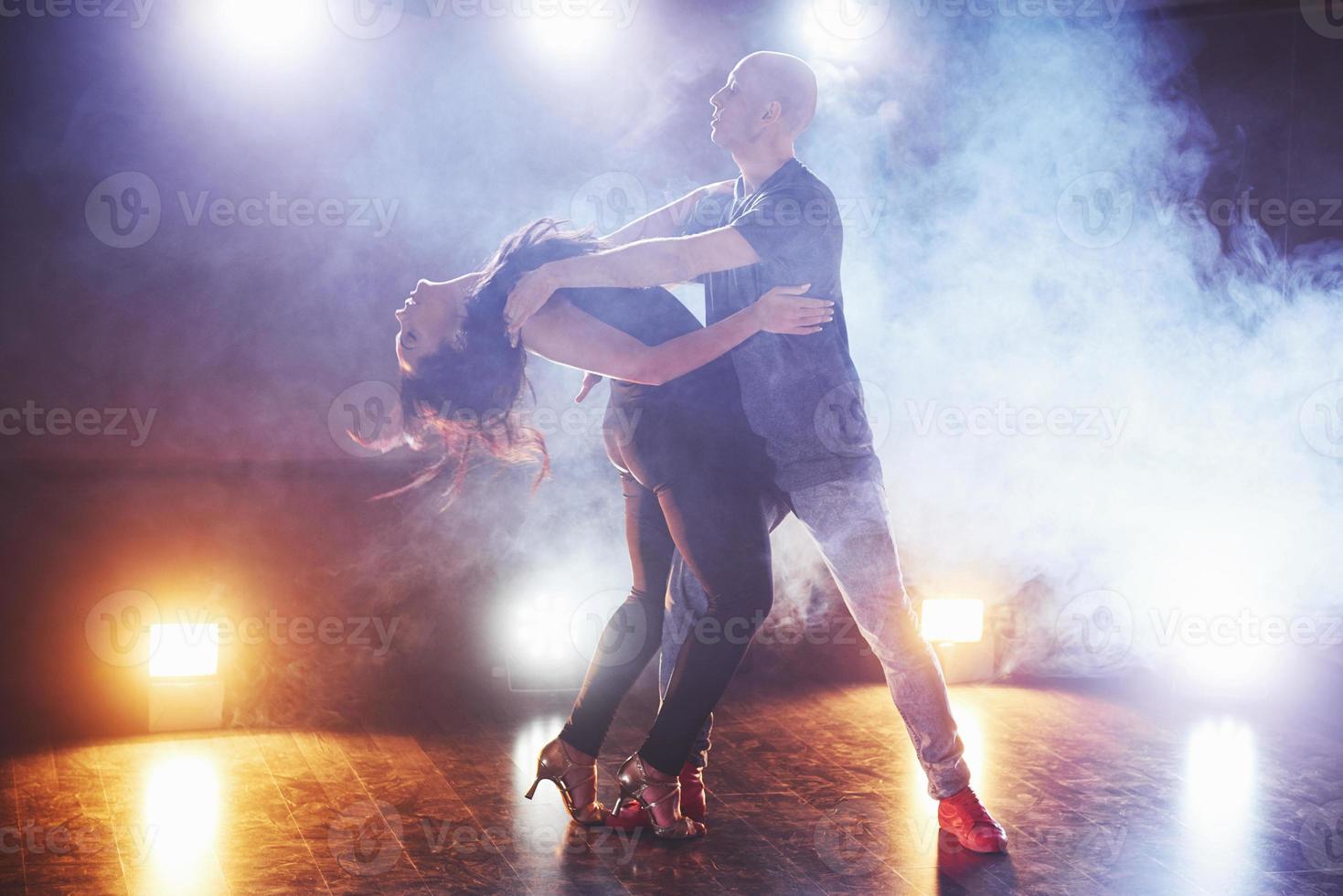 Skillful dancers performing in the dark room under the concert light and smoke. Sensual couple performing an artistic and emotional contemporary dance photo