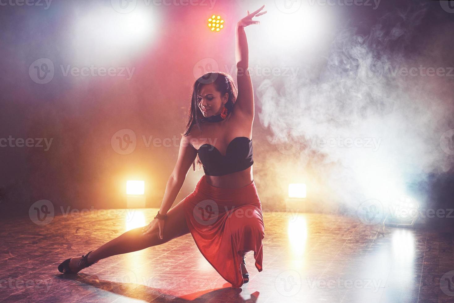 Skillful and beautiful dancer girl performing in the dark room under the concert light and smoke, performing an artistic and emotional contemporary dance photo