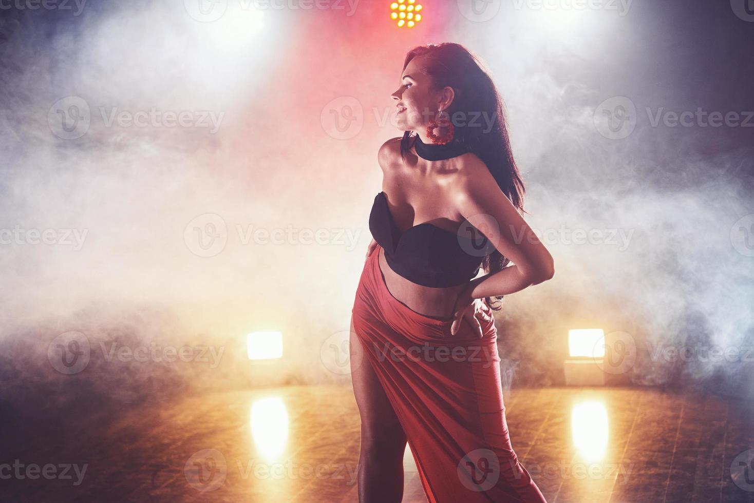 Skillful and beautiful dancer girl performing in the dark room under the concert light and smoke, performing an artistic and emotional contemporary dance photo