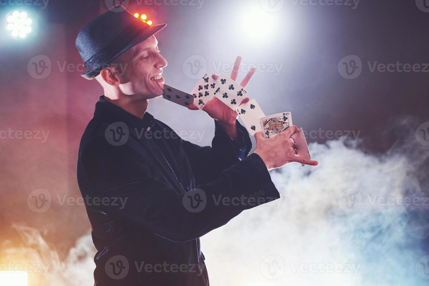 Magician showing trick with playing cards. Magic or dexterity, circus, gambling. Prestidigitator in dark room with fog photo