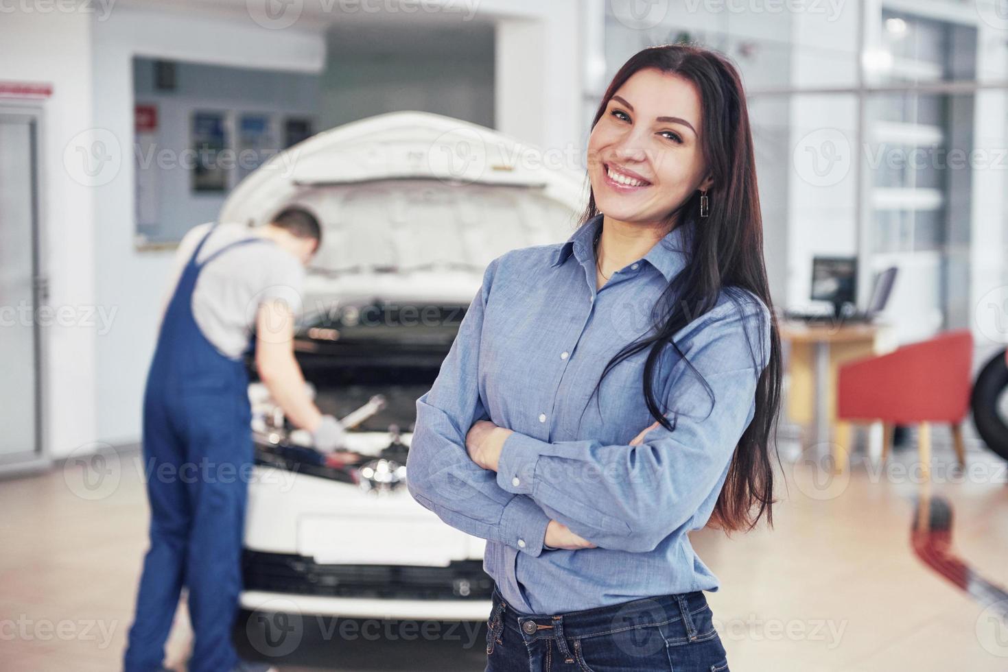 Woman at a car garage getting mechanical service. The mechanic works under the hood of the car photo