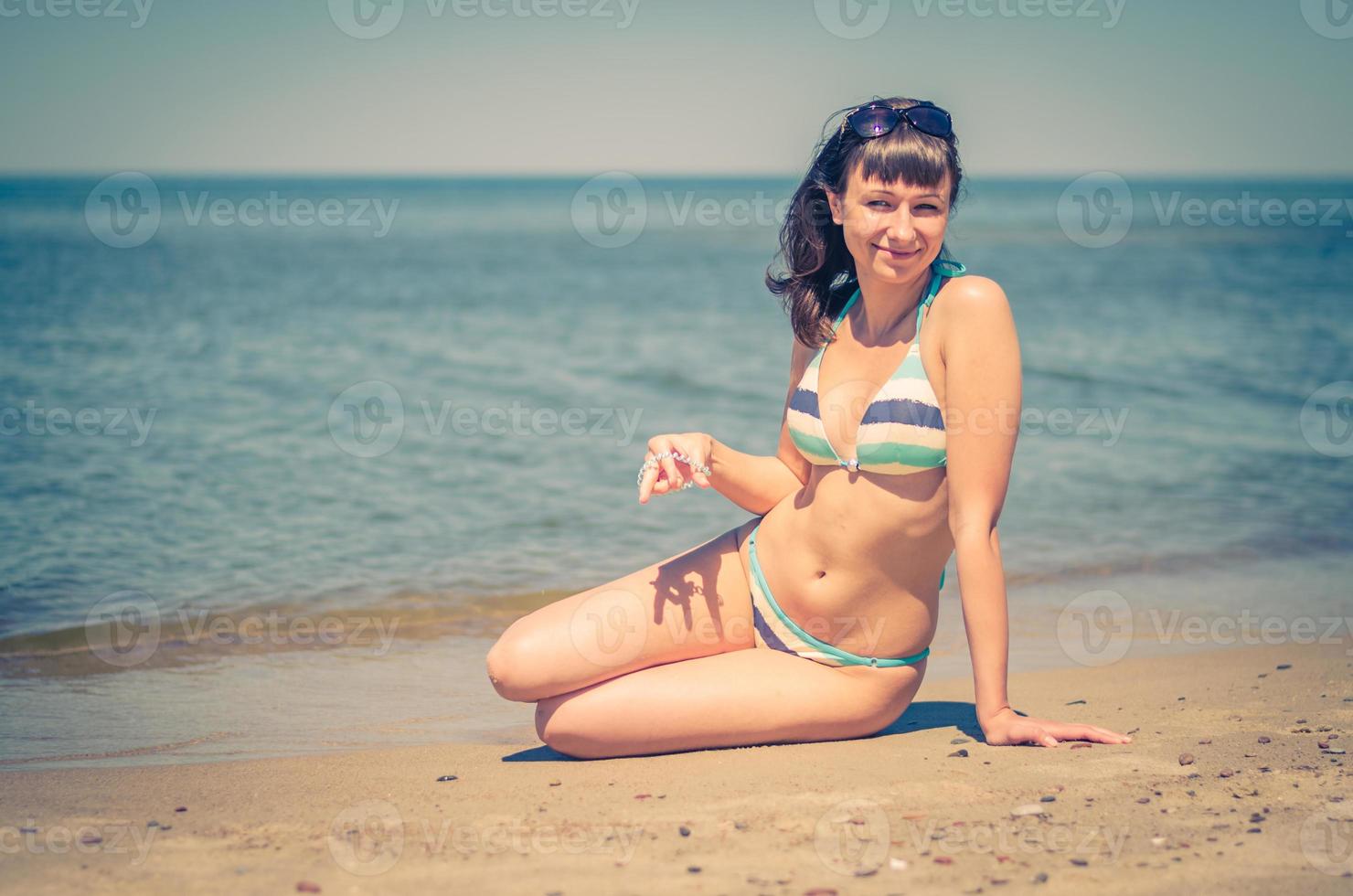 hermosa joven en bikini sentarse en la playa de arena foto