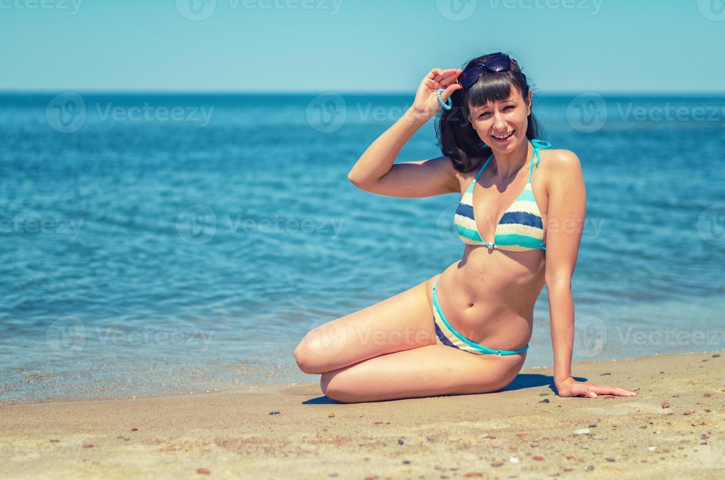 hermosa joven en bikini sentarse en la playa de arena foto