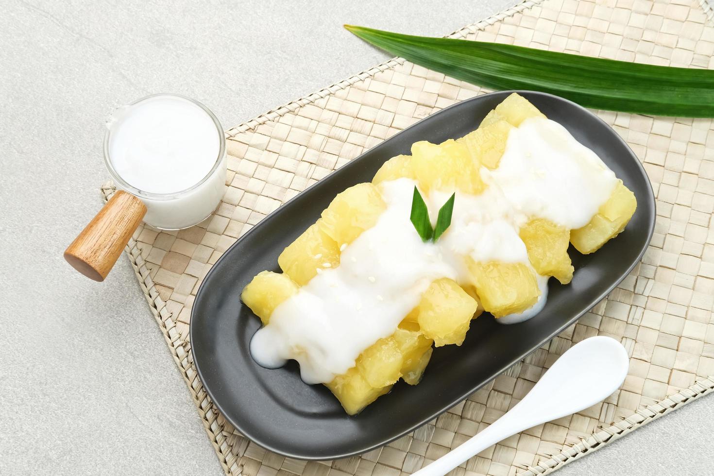 Singkong thailand, sweet cassava, made of boiled cassava, sugar and coconut milk. Served in black plate and pandan leaf photo