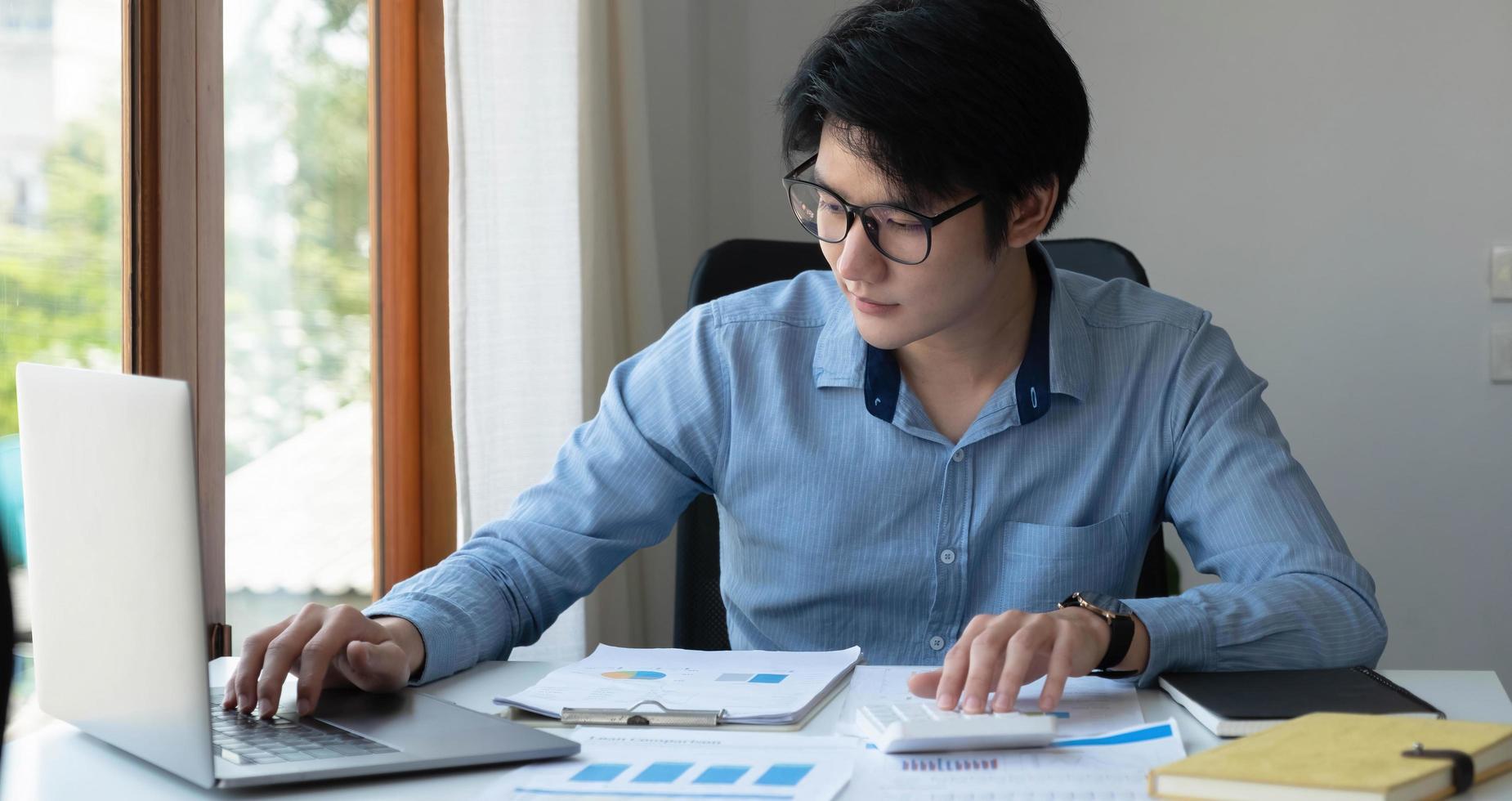 el retrato de un joven asiático independiente está trabajando en su trabajo en una tableta de computadora en una oficina moderna. hacer un informe de análisis contable datos de inversión inmobiliaria, concepto de sistemas financieros y fiscales. foto