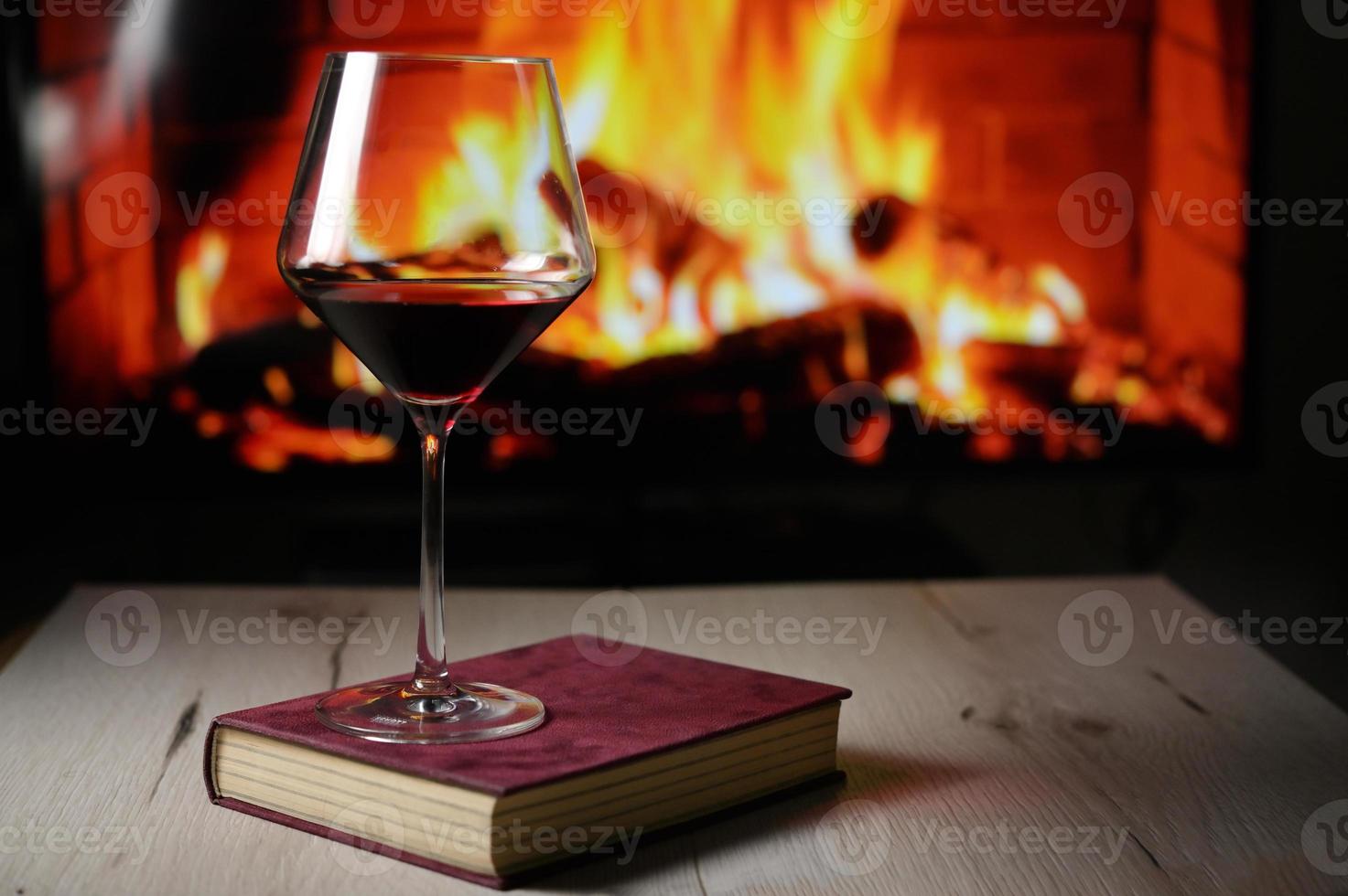 Copa de vino tinto en libro y chimenea en segundo plano. foto