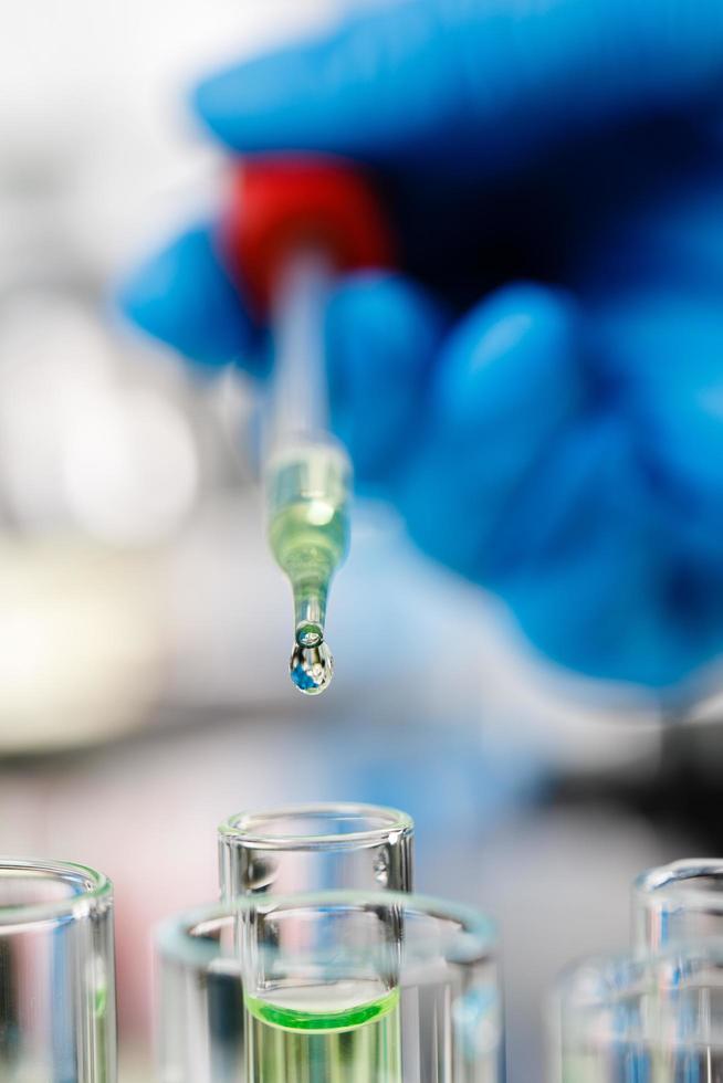 Hand wearing blue gloves holding droper and dropping water drop into test tube photo