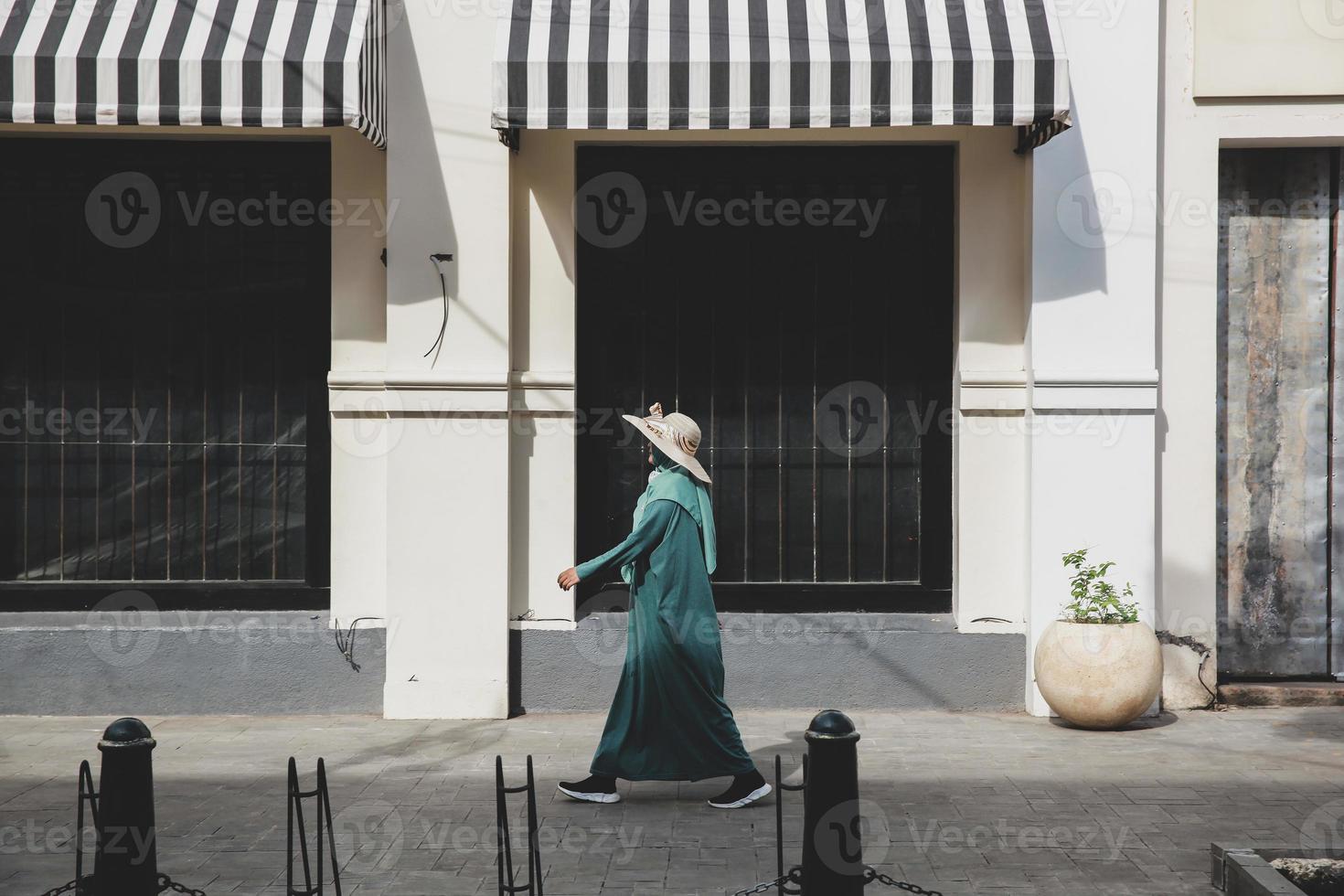 Woman in summer hat and green dress walking and passing the store on shopping area photo