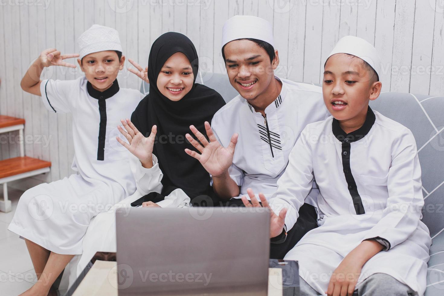 Happy Muslim family doing video conversation in front a laptop with say hi or greet gesture by hand on Eid Mubarak celebration photo