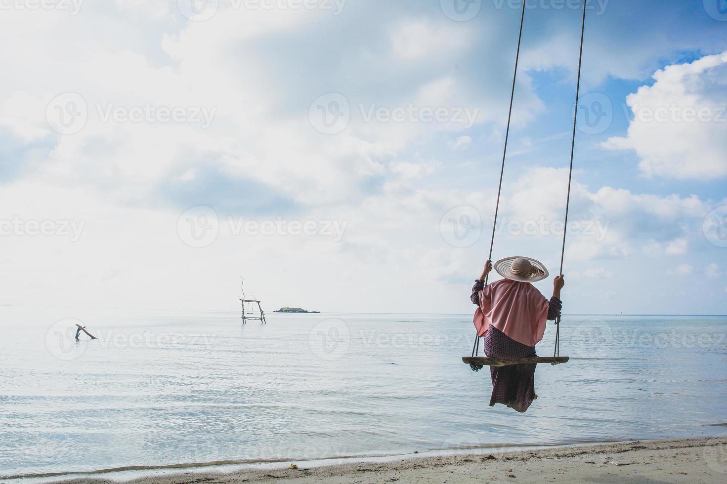 Happy young woman in summer hat swinging on the beach and enjoying sea view with copy space photo