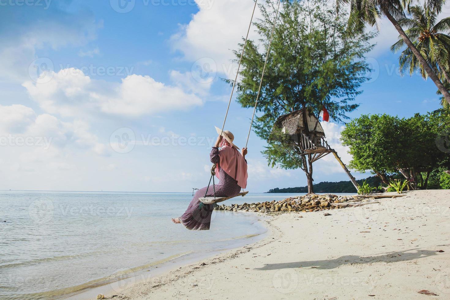 Woman in summer hat on the beach enjoying ocean view by riding a swing at Karimun Jawa photo