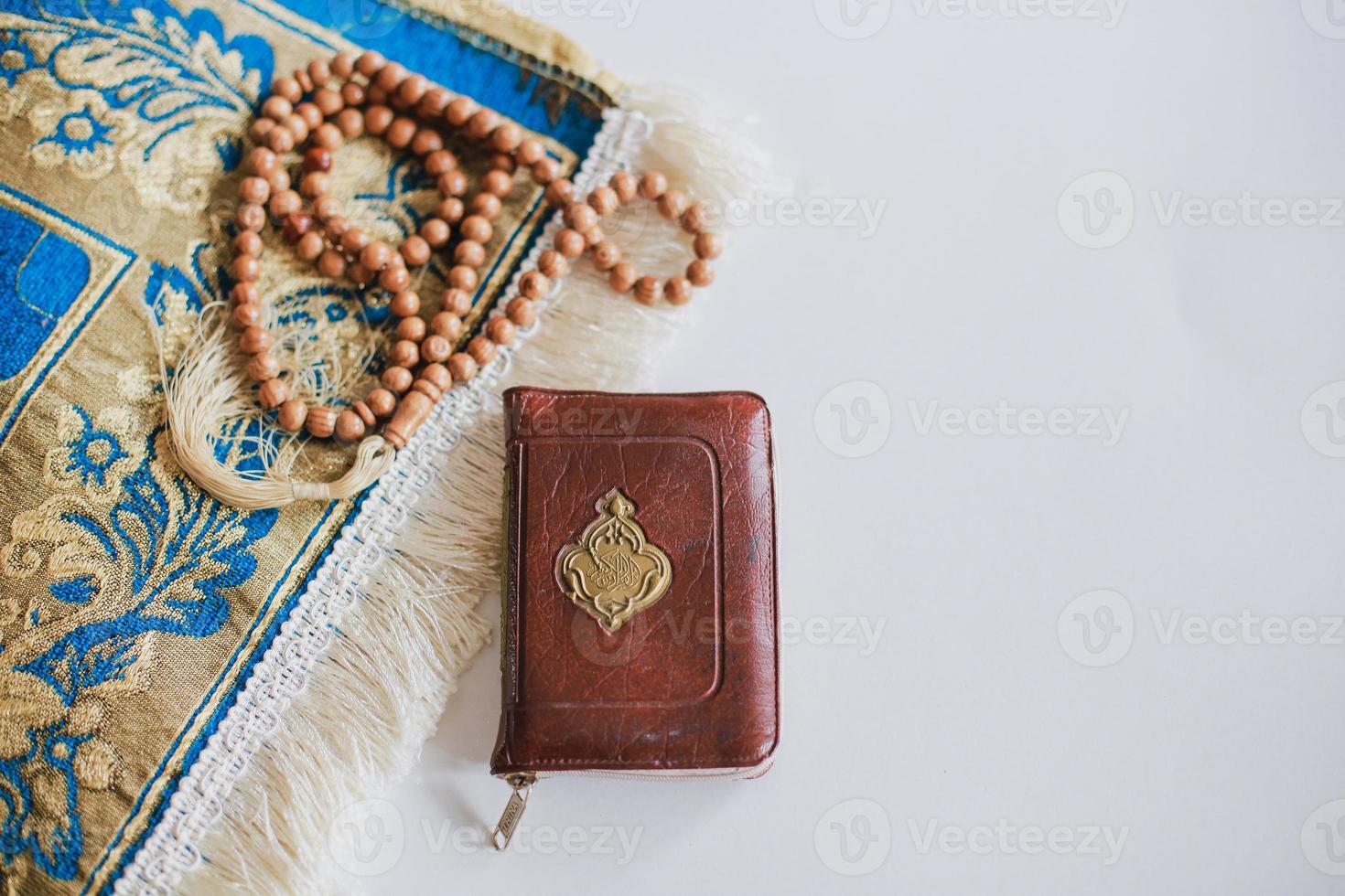 Top view of Holy Book Al Quran on the prayer mat and prayer beads with copy space. There is Arabic letter which means the holy book photo