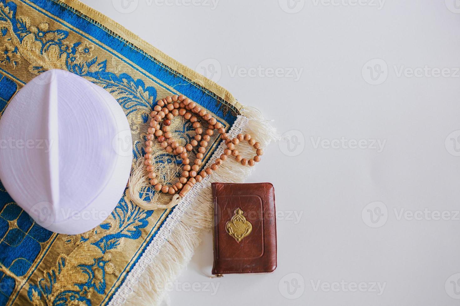Flat lay of prayer beads and cap on the prayer mat with Holy Book Al Quran. There is Arabic letter which means the holy book photo