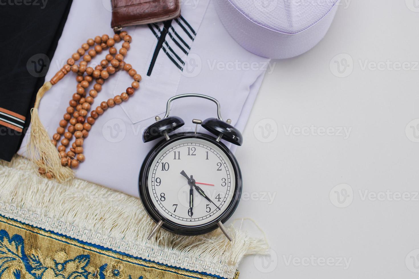 Flat lay of muslim dressed and accessories for salat with prayer beads and clock showing Fajr time pray photo