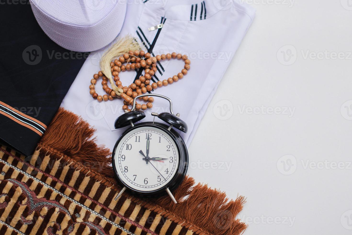 Flat lay of muslim dressed and accessories for salat with prayer beads and clock showing Asr time pray photo