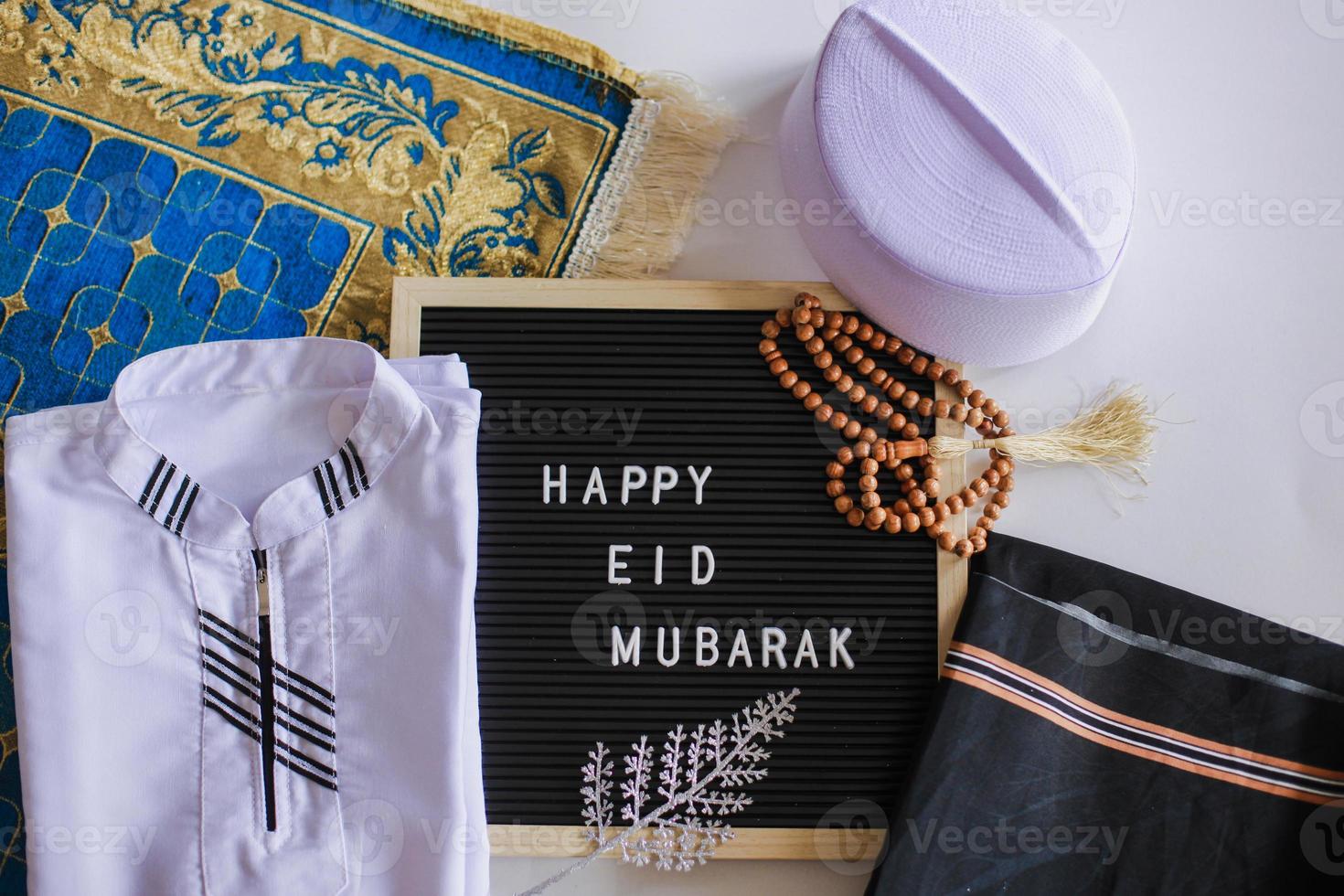 Top view of Muslim traditional dress and prayer beads on the prayer mat with letter board says Happy Eid Mubarak photo