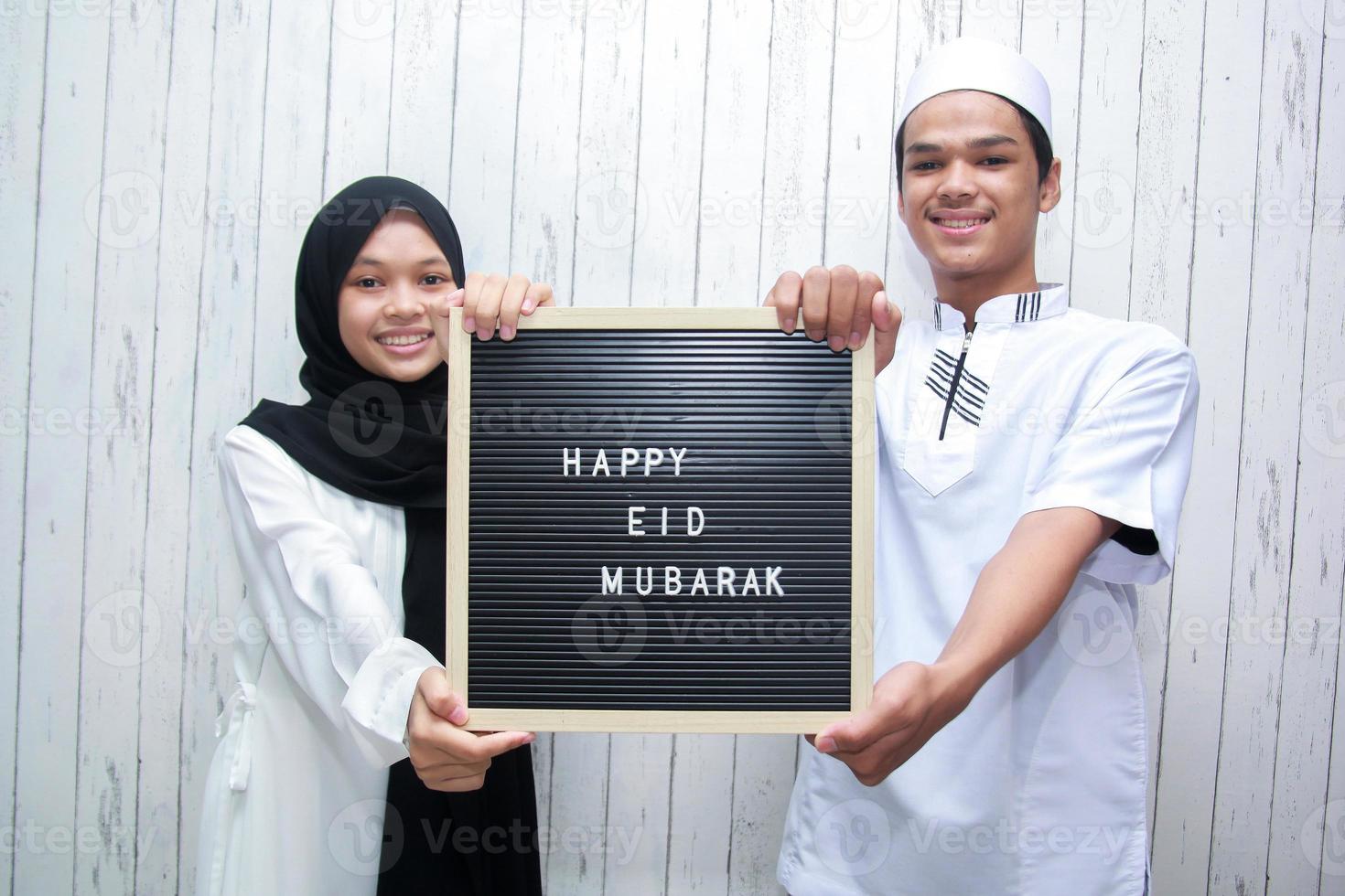 pareja musulmana asiática sosteniendo un tablero de cartas dice feliz eid mubarak foto