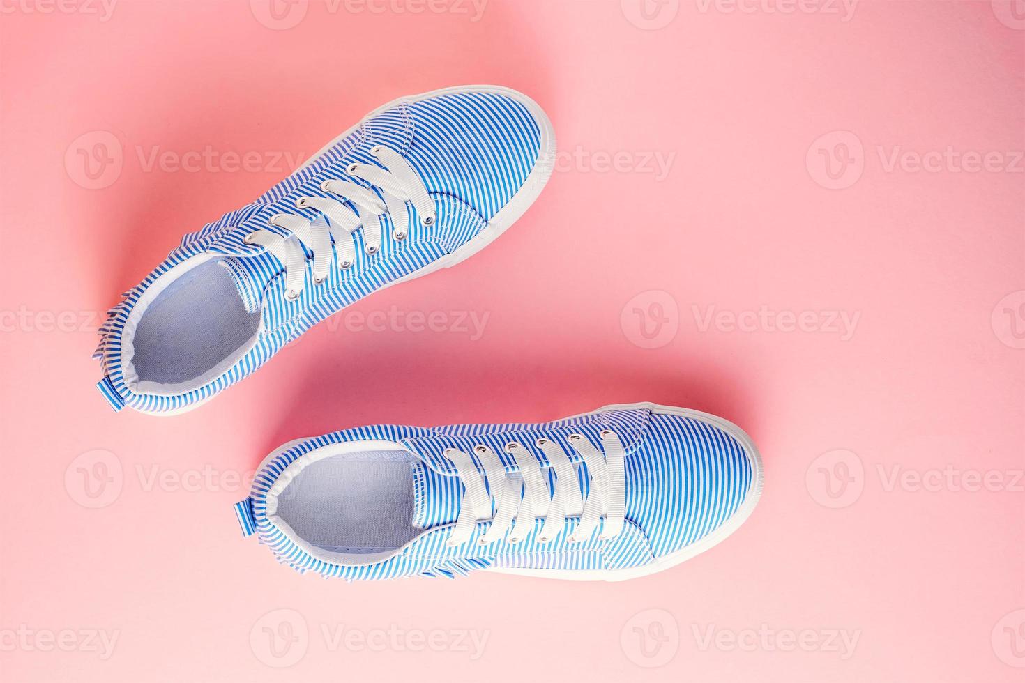 Blue striped female sneakers on pastel pink background. Flat lay, top view photo