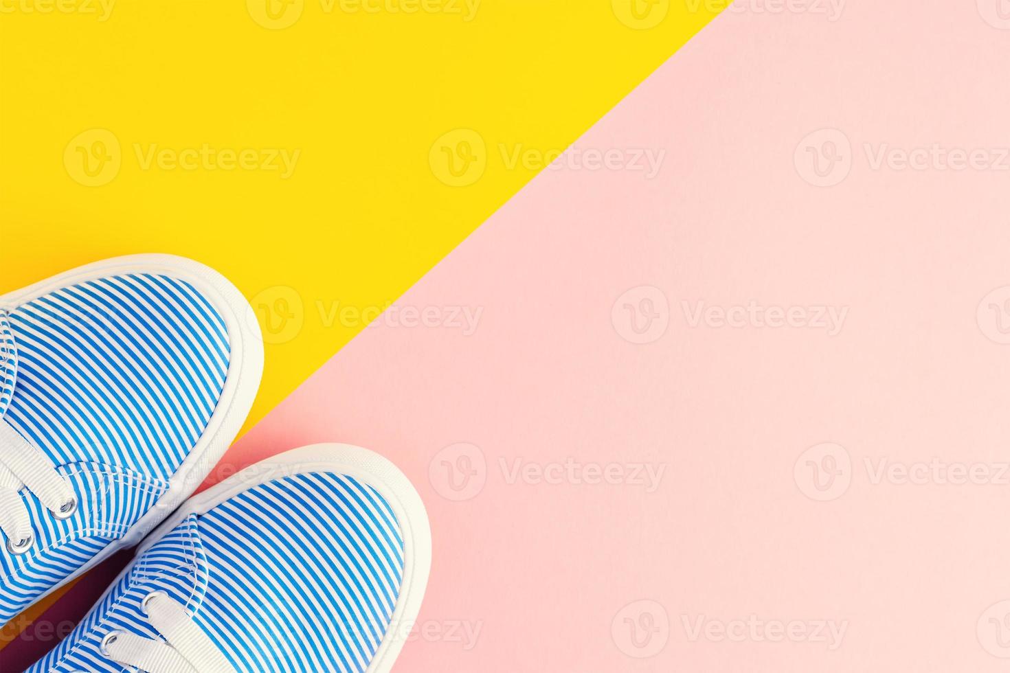 Blue striped female sneakers on pastel pink and yellow background with copy space. Flat lay, top view photo