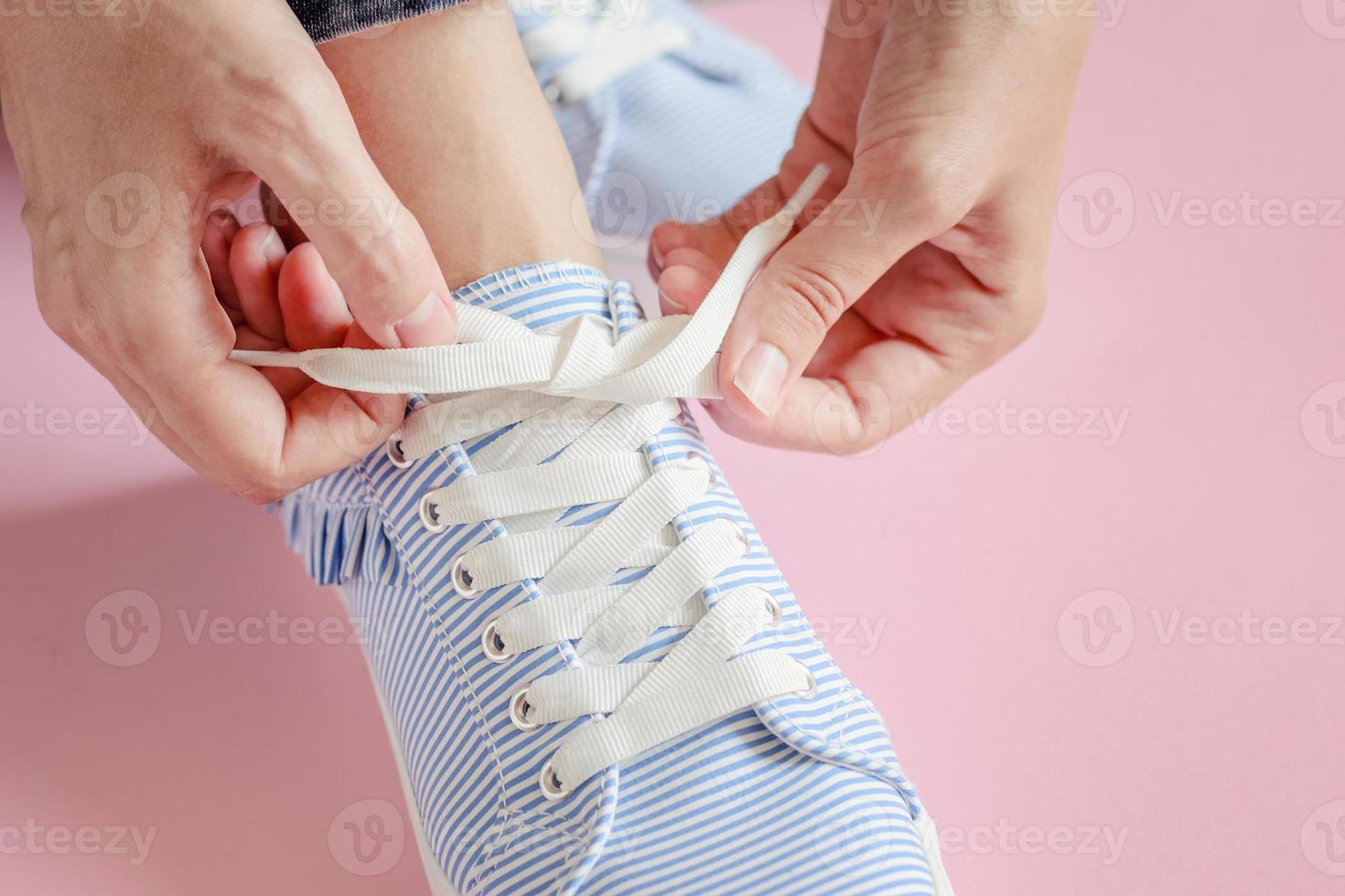woman tying shoelace at pink background close up photo