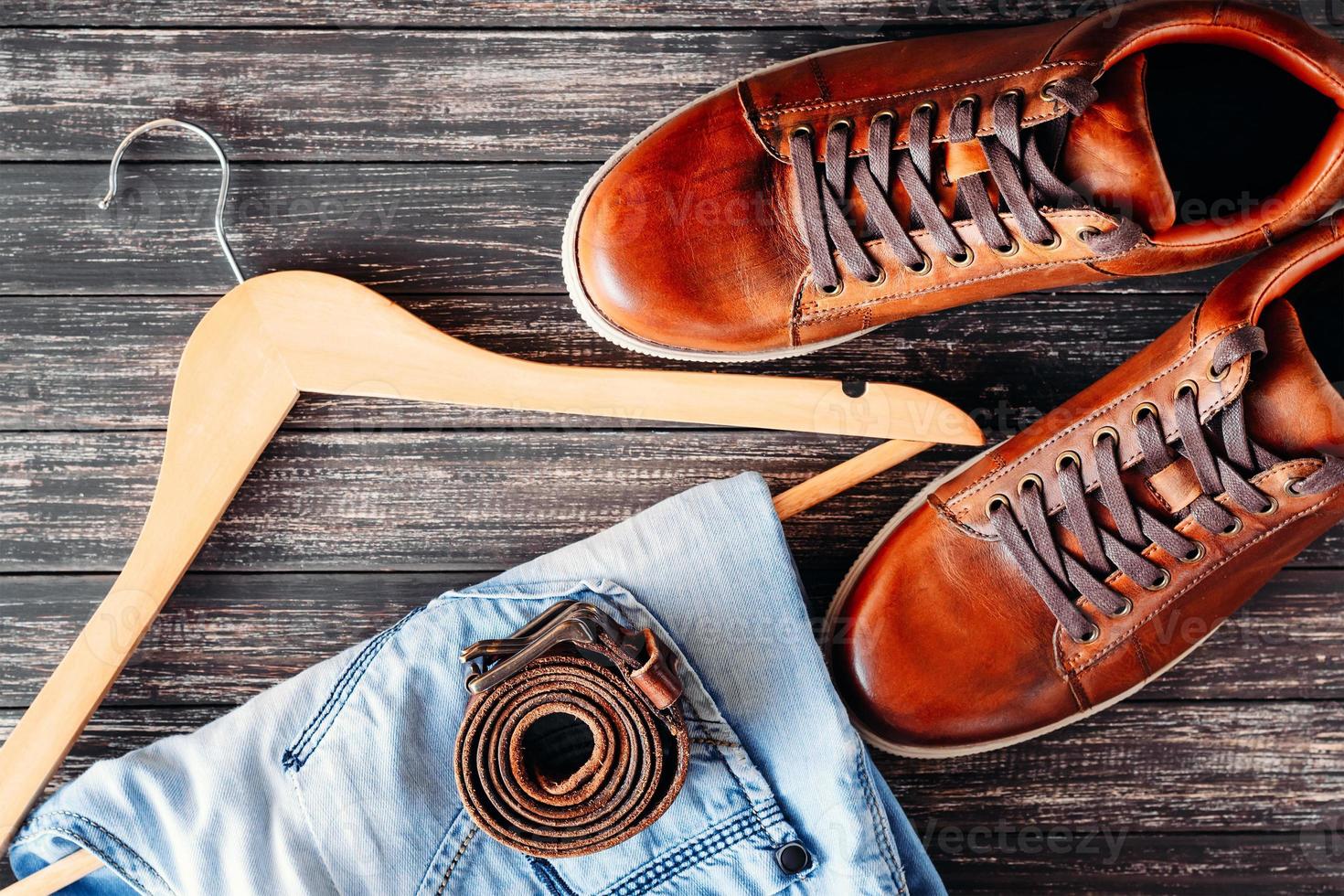 Brown leather casual shoes, jeans and belt on dark wooden background top view photo