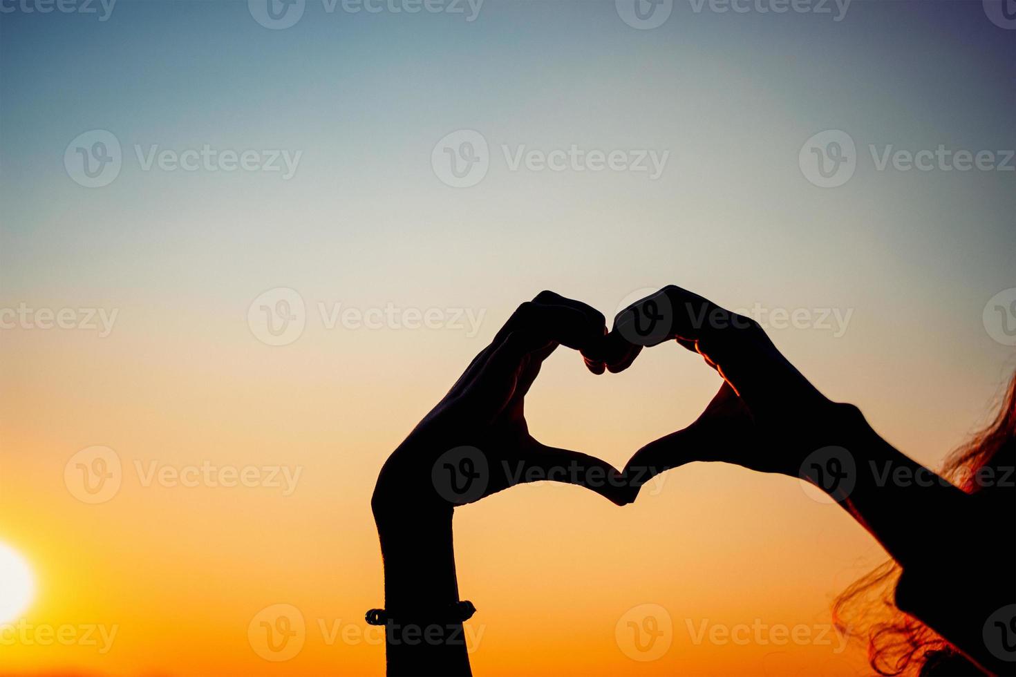 silhouette hands forming heart shape with sunset photo