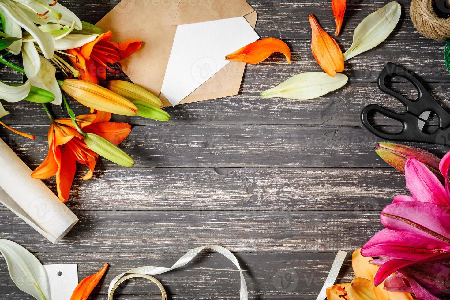 Florist work space with lilies flowers, scissors and kraft envelope flat lay, frame with copy space for design photo