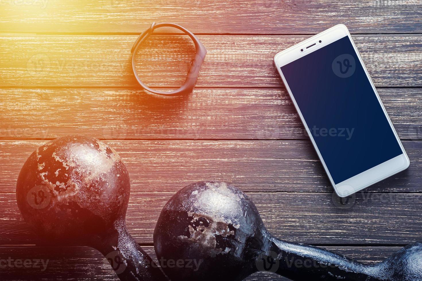 fitness tracker, smartphone and iron dumbbells on dark wooden background photo