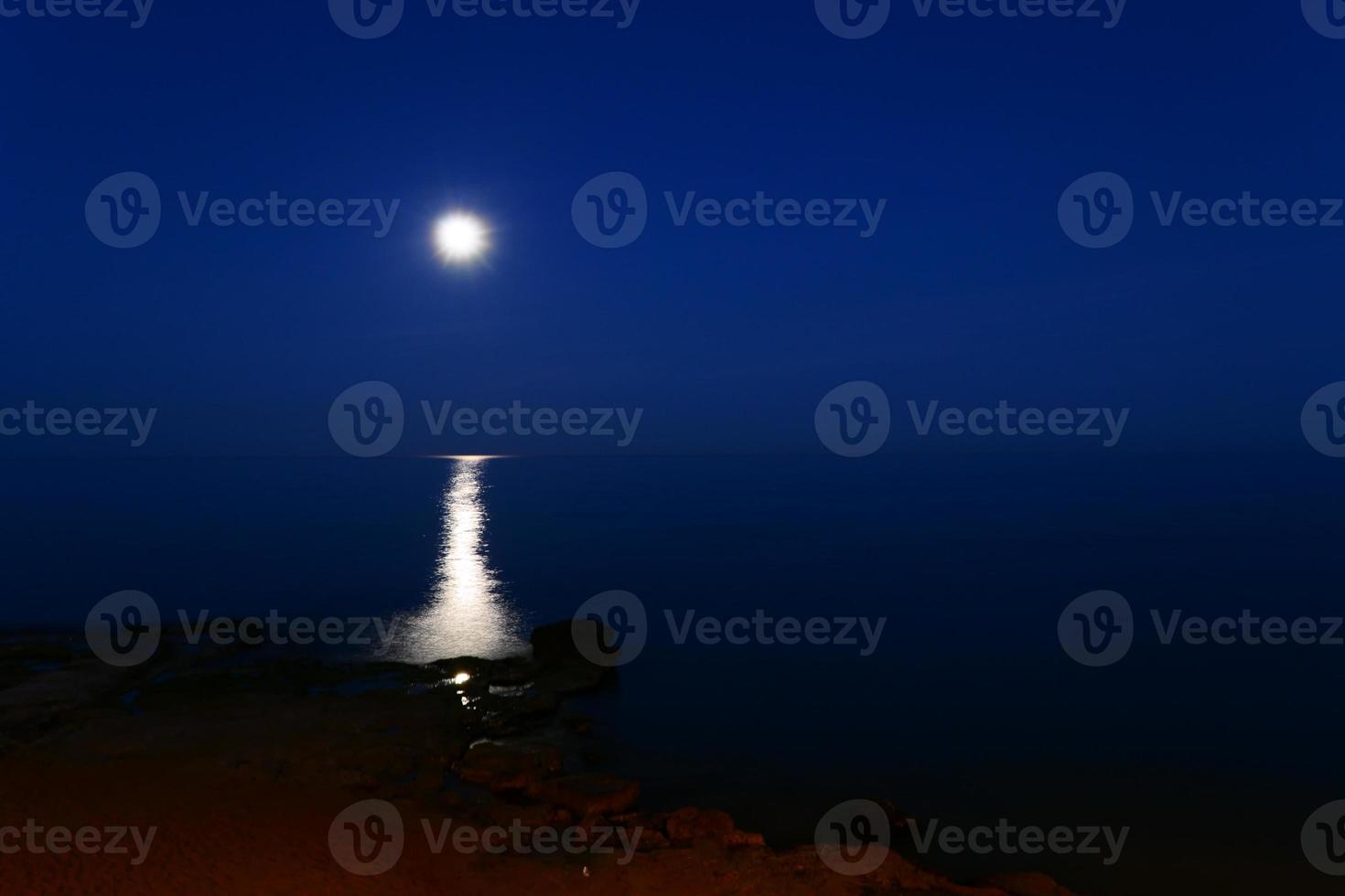 A full moon shines over the sea on a summer night. Night landscape with moon and moonbeam in the sea. photo