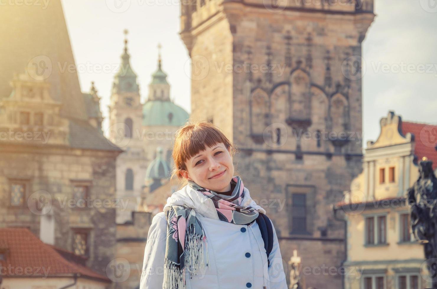 joven turista con chaqueta blanca mira la cámara y sonríe en el puente charles karluv most en el centro histórico de la ciudad de praga foto