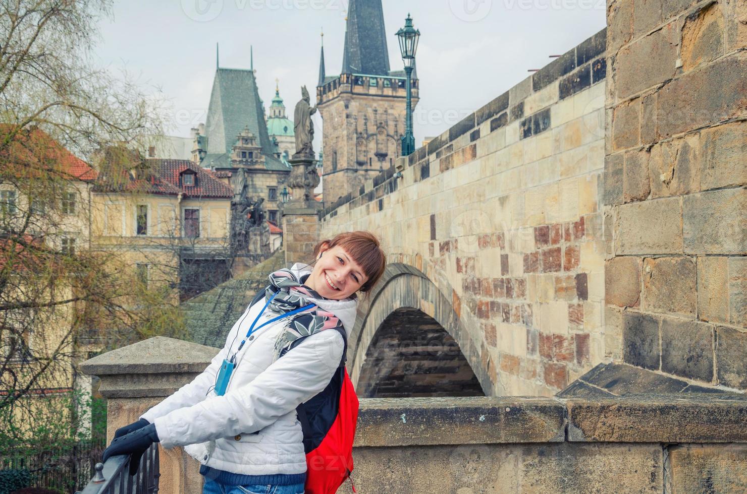 Young girl tourist with white jacket, red backpack and headphones in ears looking at camera photo