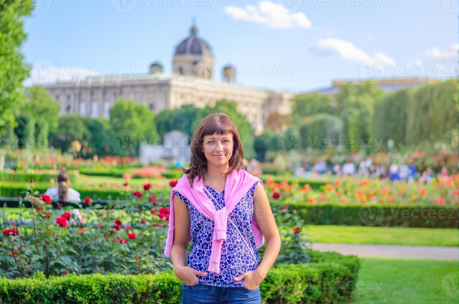 joven y hermosa chica caucásica con camisa floreada mirando a la cámara, posando y sonriendo en el parque del jardín volksgarten foto