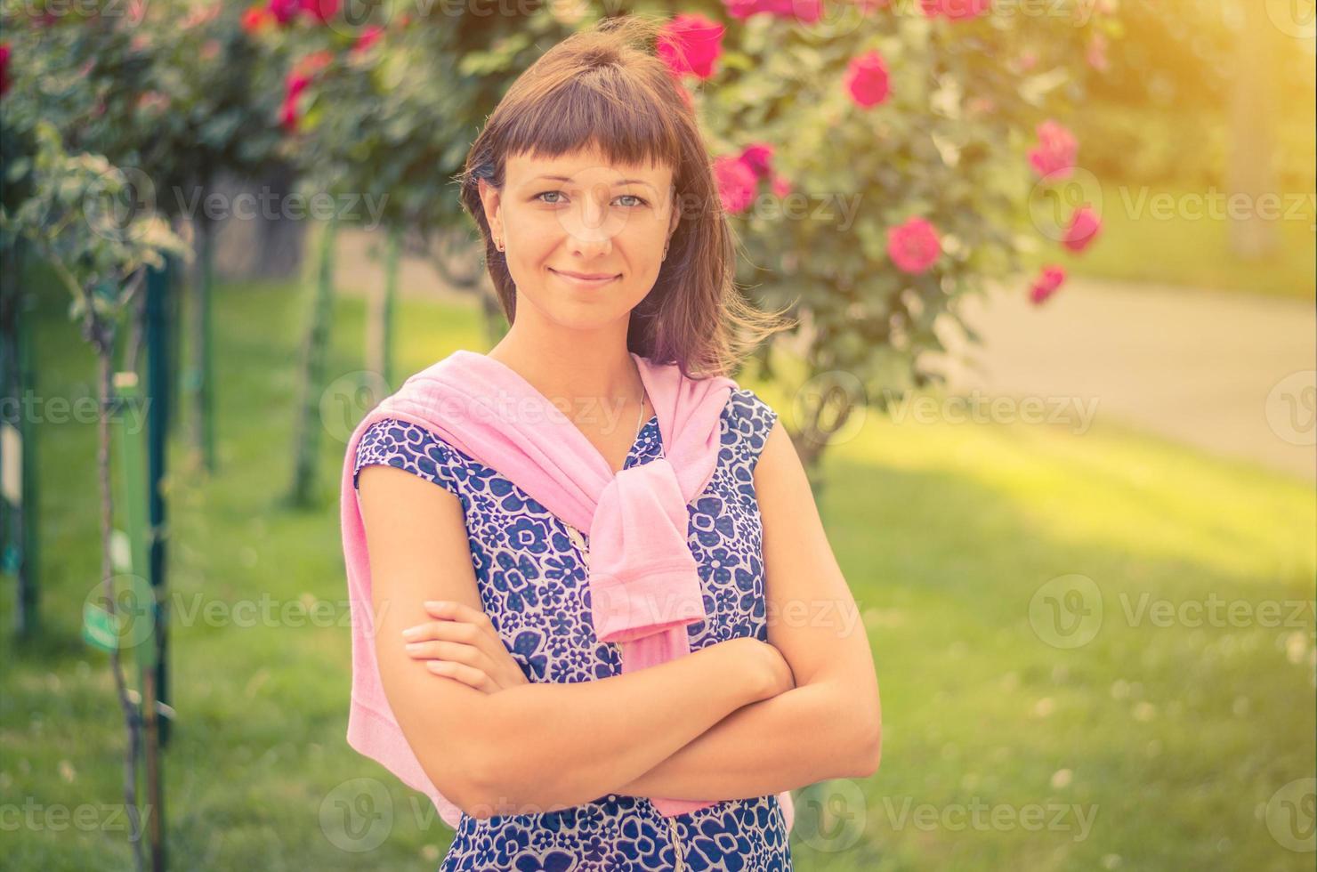 Young beautiful caucasian girl with dark hair and flowered shirt looking at camera, posing, crossing arms and smile photo