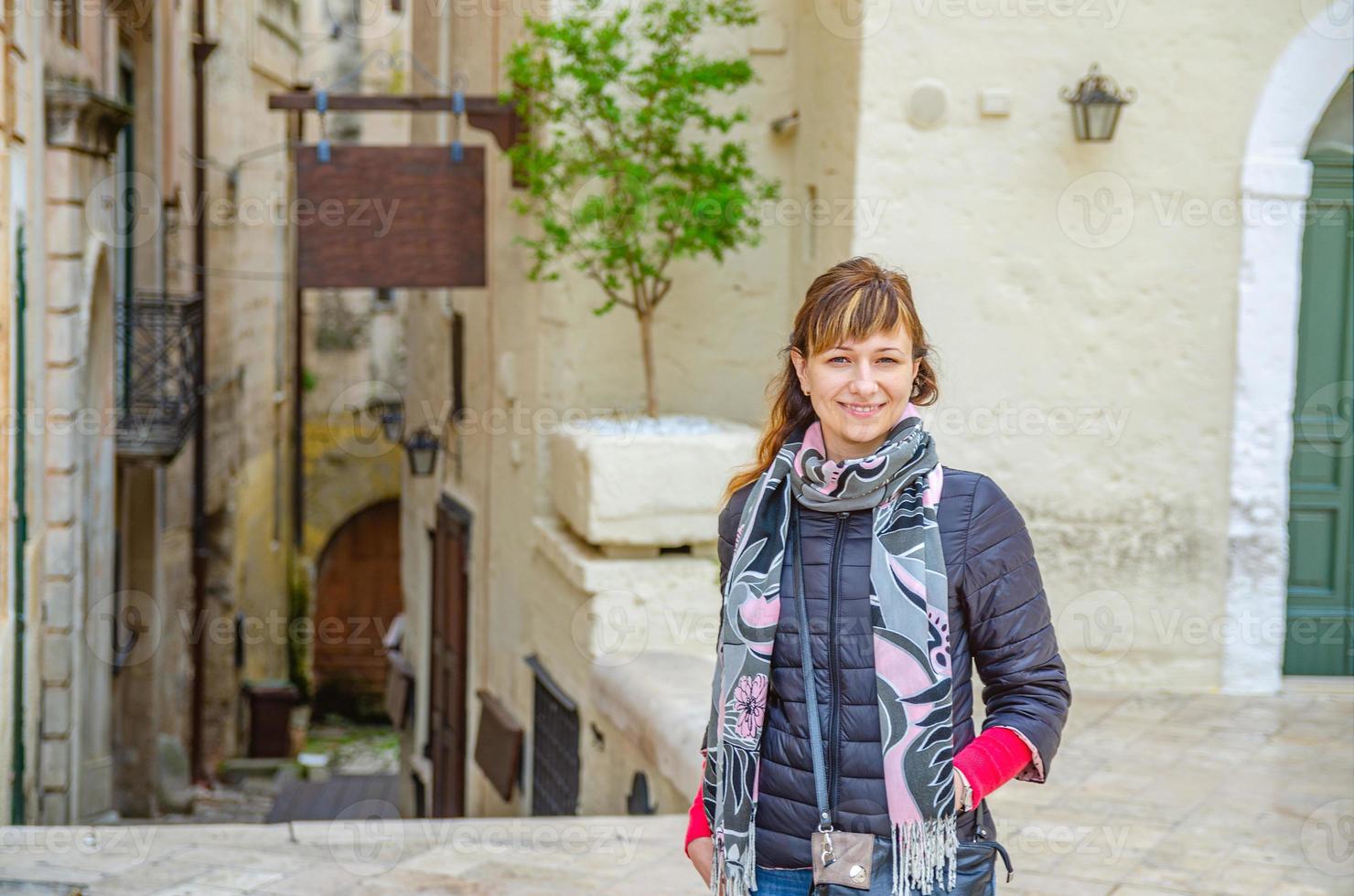 joven hermosa mujer viajera con chaqueta negra mirando a la cámara, sonriendo y posando en la calle de la ciudad de matera foto