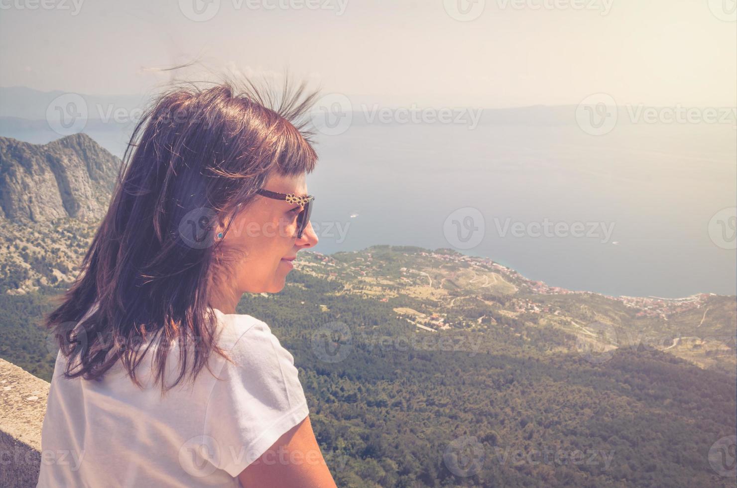 Young caucasian woman traveler with white t-shirt and sunglasses looking away distance at Adriatic sea photo