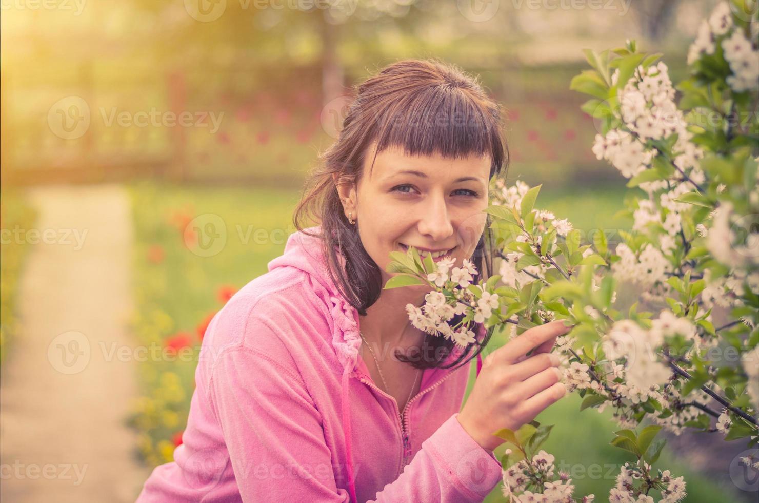 Young beautiful female woman looking at camera, smiling and smelling flowers of cherry tree blossom photo