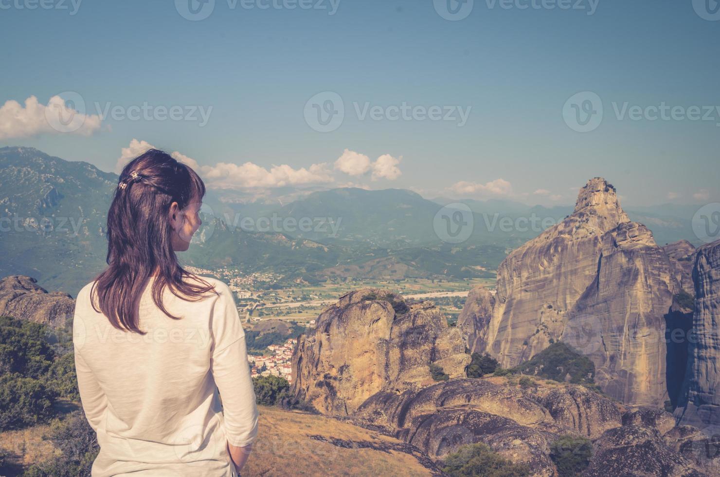 Young woman traveler with white shirt and dark hair stay and look distance away at aerial Meteora stone rocks photo