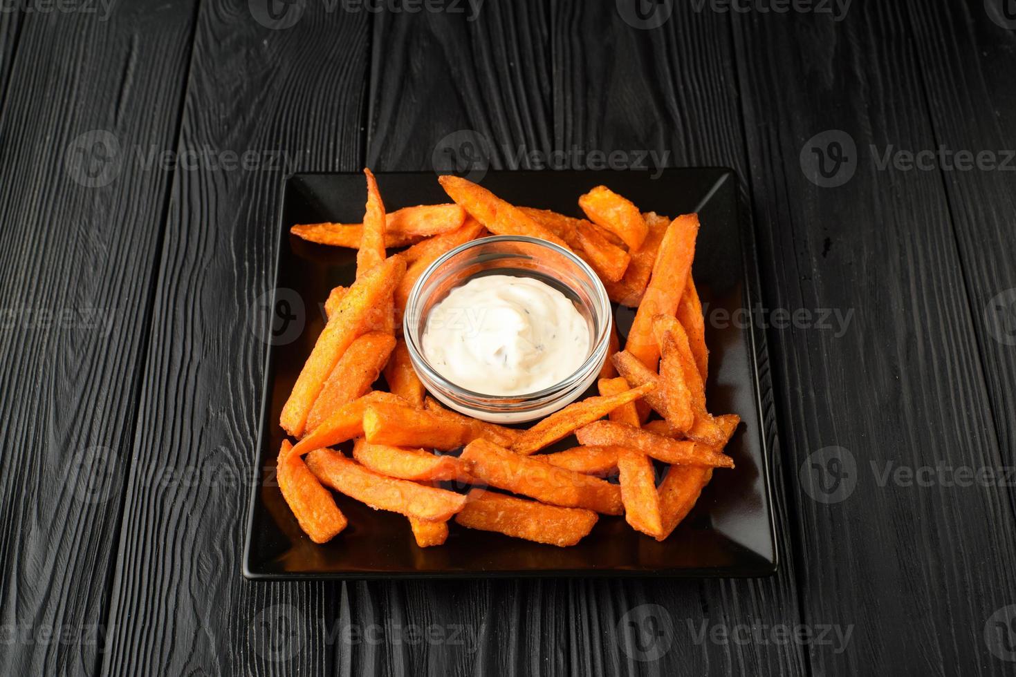 Fried sweet potatoes on a black plate with sauce on a wooden black background. photo
