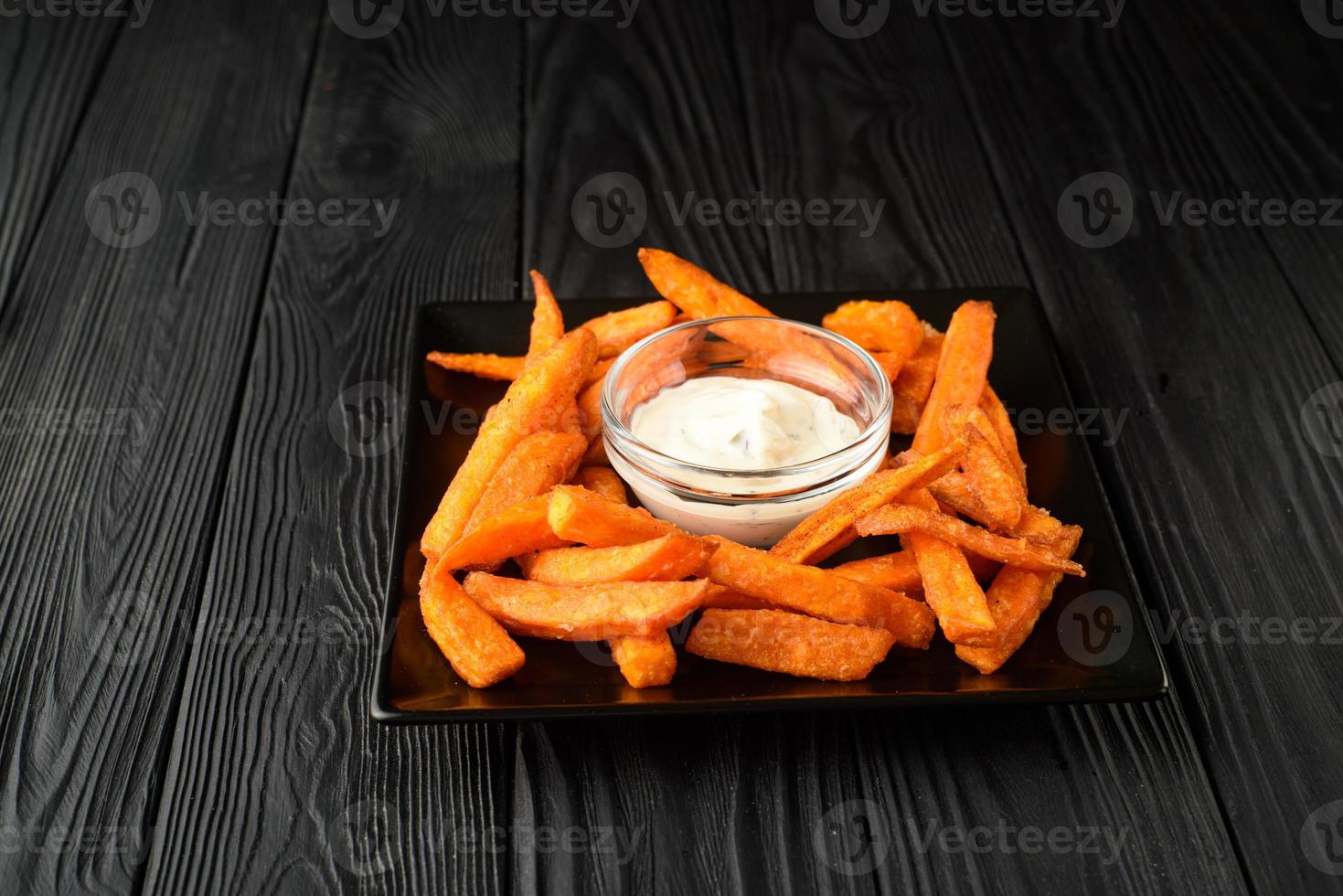 Fried sweet potatoes on a black plate with sauce on a wooden black background. photo