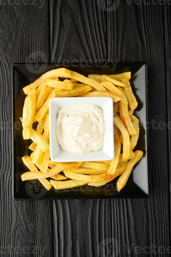 Fried French fries on a plate with sauce on a black wooden background. photo